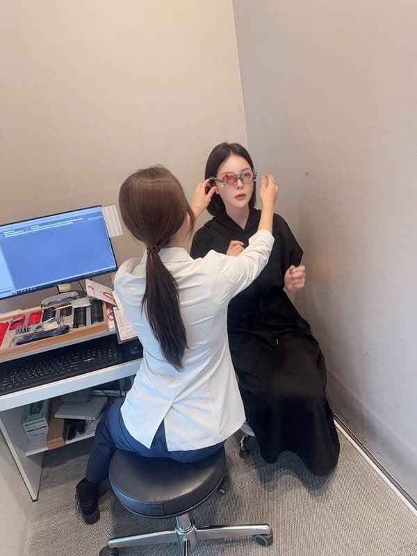 趙心姸穿黑色洋裝坐在驗光室，一位穿白袍的檢查人員正替她調整試鏡架，左側是電腦螢幕和整盒試片