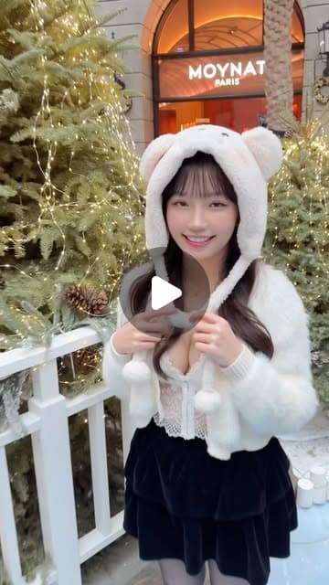 MiO 戴著白色毛絨熊耳帽、穿白色外套，站在掛滿燈飾的聖誕樹前微笑的影片封面