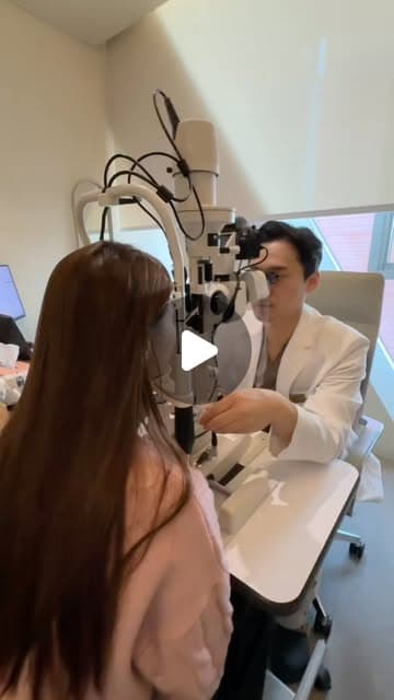 穿粉紅色上衣的長髮女生坐在裂隙燈前，穿白袍的醫師正透過儀器為她檢查眼睛