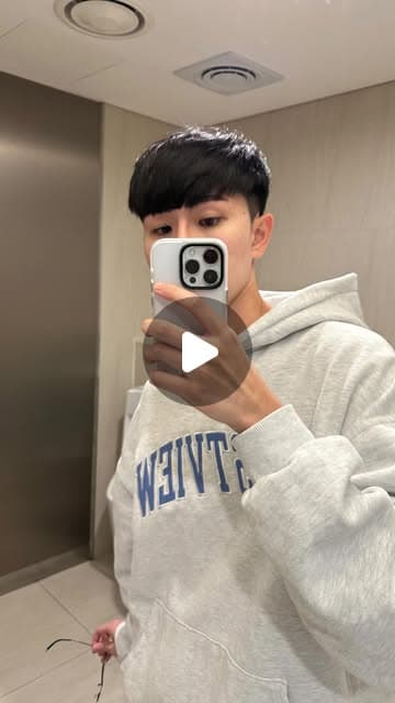 尼克穿灰色連帽上衣對著鏡子用手機自拍，另一隻手拿著摘下來的眼鏡