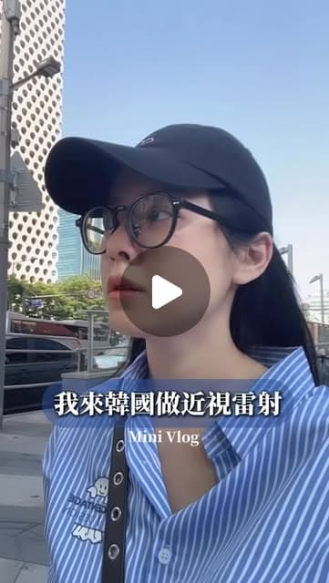 戴黑色棒球帽和圓框眼鏡、穿藍白條紋襯衫的Joanne站在首爾街頭高樓前，畫面字幕寫著「我來韓國做近視雷射」與「Mini Vlog」