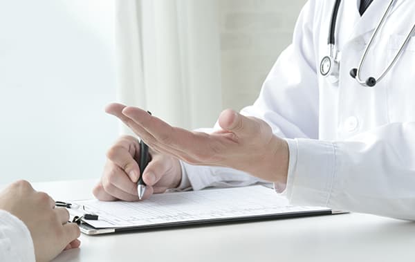 白衣の医師が机をはさんで患者に説明している場面