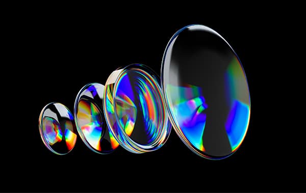 A row of clear optical lenses of increasing size on a black background, catching rainbow reflections