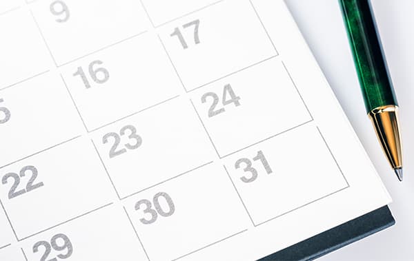 Close-up of a white desk calendar with the dates 16 to 31 and a green fountain pen resting beside it